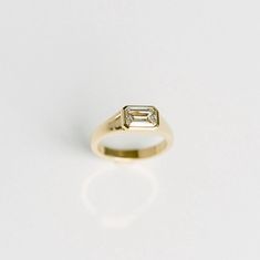 a yellow gold ring with a baguette cut diamond set in the center, on a white background