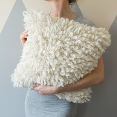 a woman holding a pillow made out of white yarn