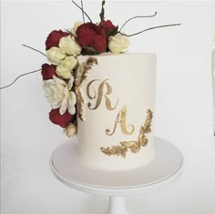 a white and gold wedding cake with red roses on the top is next to a bottle of champagne