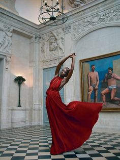 a woman in a red dress is standing on a checkered floor with her arms up