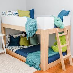 a child's bunk bed with blue and green pillows on the bottom, next to a wooden ladder