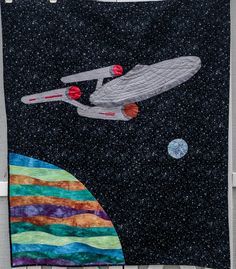 a quilted wall hanging with a star trek ship and planets in the sky on it