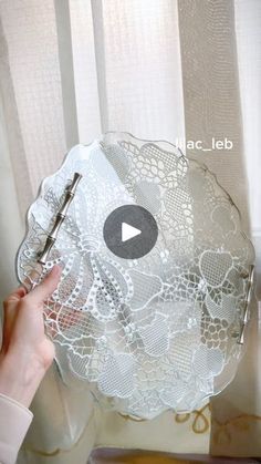 a person is holding a white lace doily with scissors in front of a window