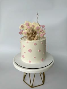 a white cake with pink hearts and a teddy bear in the middle on a stand