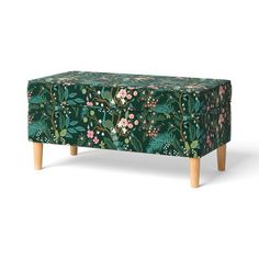 an upholstered footstool with flowers and leaves on green fabric, in front of a white background