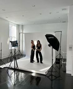 two women are standing in front of a white backdrop with black lights and umbrellas