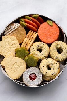 a metal bowl filled with cookies, pretzels and crackers next to carrots