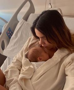 a woman holding a baby in her arms while sitting on a bed next to an adult