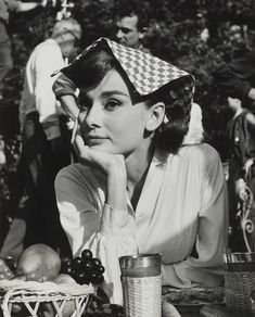 a woman sitting at a table with grapes and an apple in front of her, wearing a checkered hat