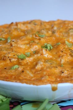 a casserole dish with cheese and green onions in it on a colorful table cloth