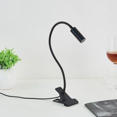 a wine glass sitting next to a lamp on top of a white table with a book