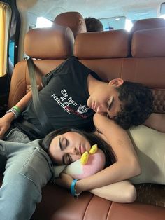 two people laying on the back of a car with their arms around each other as they sleep