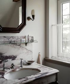 a bathroom sink with marble counter top next to a window and a mirror above it