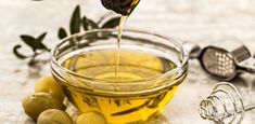 olive oil being poured into a glass bowl filled with olives and an olive peel