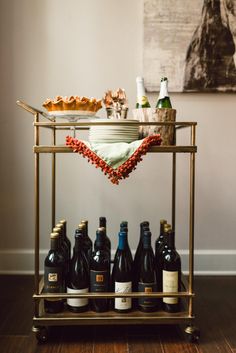 a bar cart filled with bottles of wine on top of a hard wood floor next to a wall