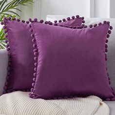 two purple pillows sitting on top of a couch next to a potted palm tree