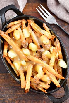 a skillet filled with french fries covered in gravy next to a fork