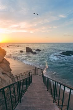 stairs lead down to the beach as the sun sets over the ocean in the background