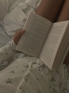 a woman laying in bed with her legs crossed and holding an open book above her head