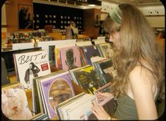 a woman looking at records in a record store with many covers on the shelves and posters behind her