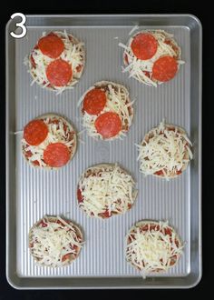 six mini pizzas on a baking sheet with cheese and pepperoni sprinkled on top