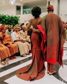 two women in red and orange dresses are walking down the runway with other people seated behind them