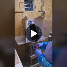 a person in blue gloves is working on a piece of wood with a machine behind him