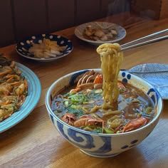 a bowl of soup with chopsticks sticking out of it and other dishes in the background