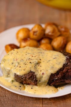 a white plate topped with meat covered in gravy next to some fried potatoes