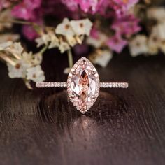 a pink diamond ring sitting on top of a wooden table next to purple and white flowers