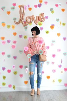 a woman standing in front of a wall with hearts and the word love on it