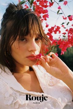 a beautiful young woman posing in front of red flowers with her hand on her face