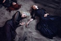 three women laying on the sand in dresses