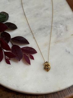 a gold necklace with a small pendant on top of it next to some leaves and a plant