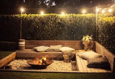 a wooden bench sitting in the middle of a lush green yard with lights strung over it