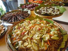 many plates of food on a table with people in the background and one plate filled with noodles