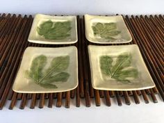 four plates with leaf designs on them sitting on a bamboo mat