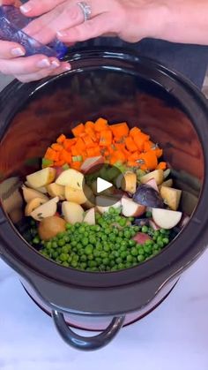 a person holding a cell phone in front of a pot filled with vegetables and peas