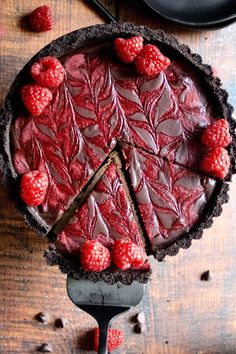 a chocolate tart with raspberries on top and one slice missing from it