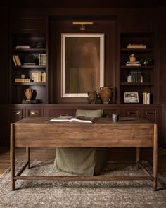 a wooden desk sitting in the middle of a living room next to a book shelf