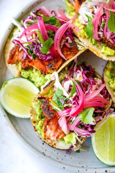 some tacos are on a white plate with limes and red onion slaw