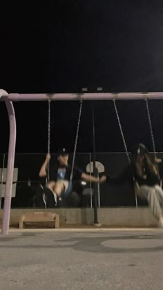 two people sitting on swings at night with no one in the photo watching them play