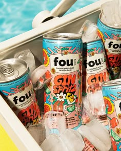 four cans of soft drinks are in an ice chest next to a pool with blue water