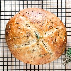 a loaf of bread sitting on top of a cooling rack next to a sprig of rosemary