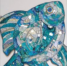 a blue fish made out of glass and silver beads on a white surface with an eye in the center