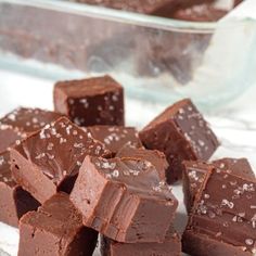 a pile of chocolate fudges sitting on top of a white plate next to a glass dish