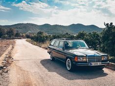 an old mercedes parked on the side of a road in front of some hills and trees