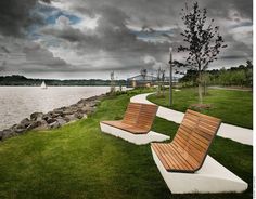 two wooden benches sitting next to each other on top of grass covered ground near water