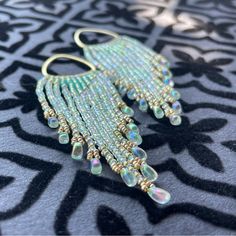 a pair of earrings sitting on top of a black and white table cloth with gold beads