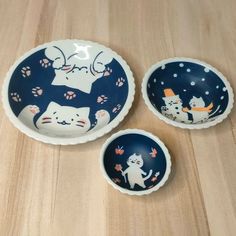 three bowls with cats painted on them sitting on a wooden table next to each other